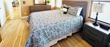 A bedroom with a bed, a nightstand, a dresser, a ceiling fan, and a window with blinds.