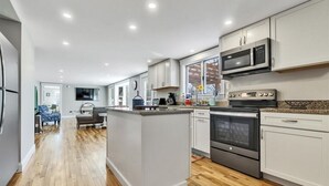 A modern kitchen with white cabinets, a central island, stainless steel appliances, and a wooden floor. - Walk To Wells Harbor! Ping Pong Table & Large Yard (Wells)