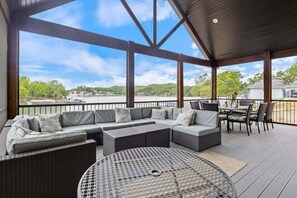 A covered outdoor seating area with a large sectional sofa, a round metal table, and a dining table with chairs. - Luxury Home on Cove with Boat Slip, Waterslides, and Jump Deck (Linn Creek)