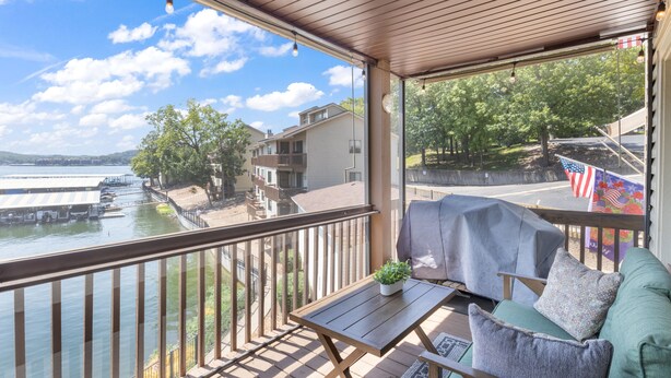 A balcony with a view of a lake, a covered grill, and a seating area with a cushion. - Lakefront Couple Retreat near Hot Spots and Dining (Lake Ozark)
