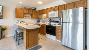 A modern kitchen with wooden cabinets, stainless steel appliances, and a central island with bar stools. - Lakefront Couple Retreat near Hot Spots and Dining (Lake Ozark)
