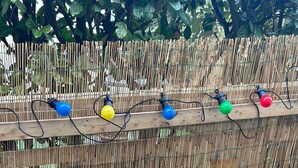 Une clôture en bambou agrémentée de guirlandes lumineuses colorées.