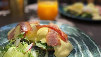A plate of food with bacon and greens, a glass of orange juice, and a potted plant in the background.