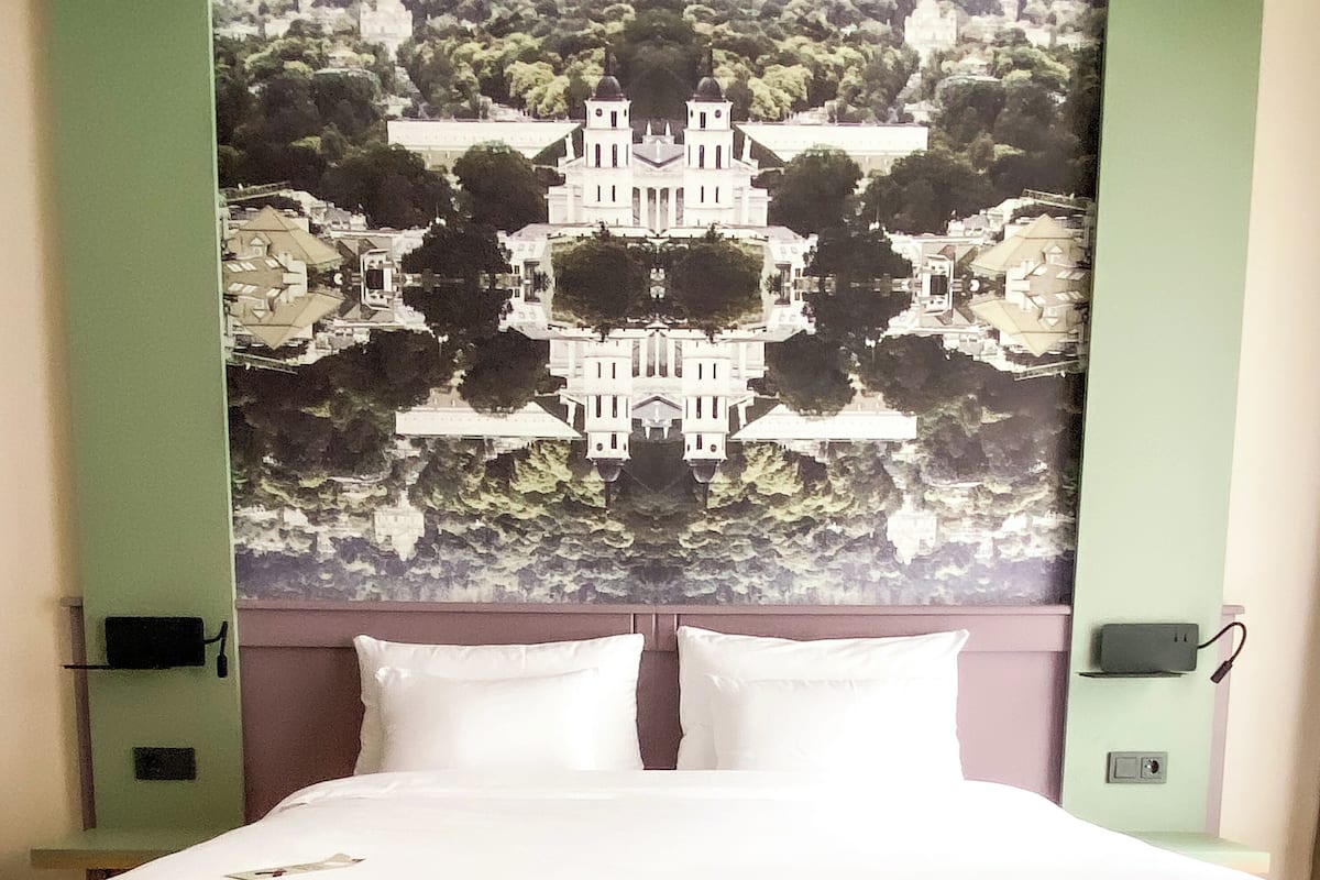 A bed with white linens, a headboard with a symmetrical design, and two bedside tables with lamps.