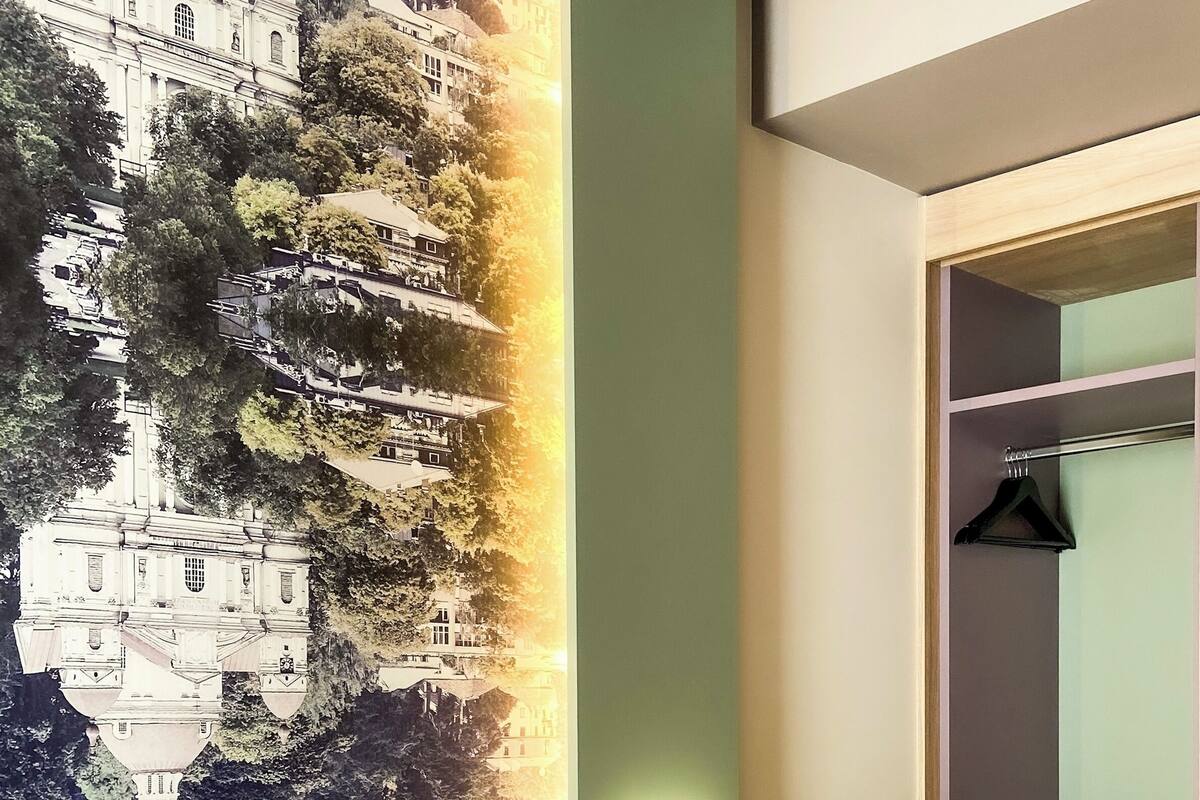 A hotel room with a bed, a wall-mounted TV, a wardrobe, and a large mural on the wall.