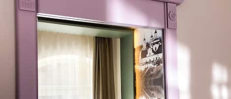 Una habitación de hotel con cama, cortinas, mesita de noche y una lámpara fijada a la pared.