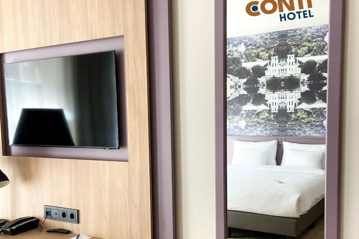 A hotel room with a mounted television, a desk with a telephone and a notepad, and a poster of the hotel.