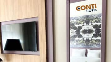 A hotel room with a mounted television, a desk with a telephone and a notepad, and a poster of the hotel.