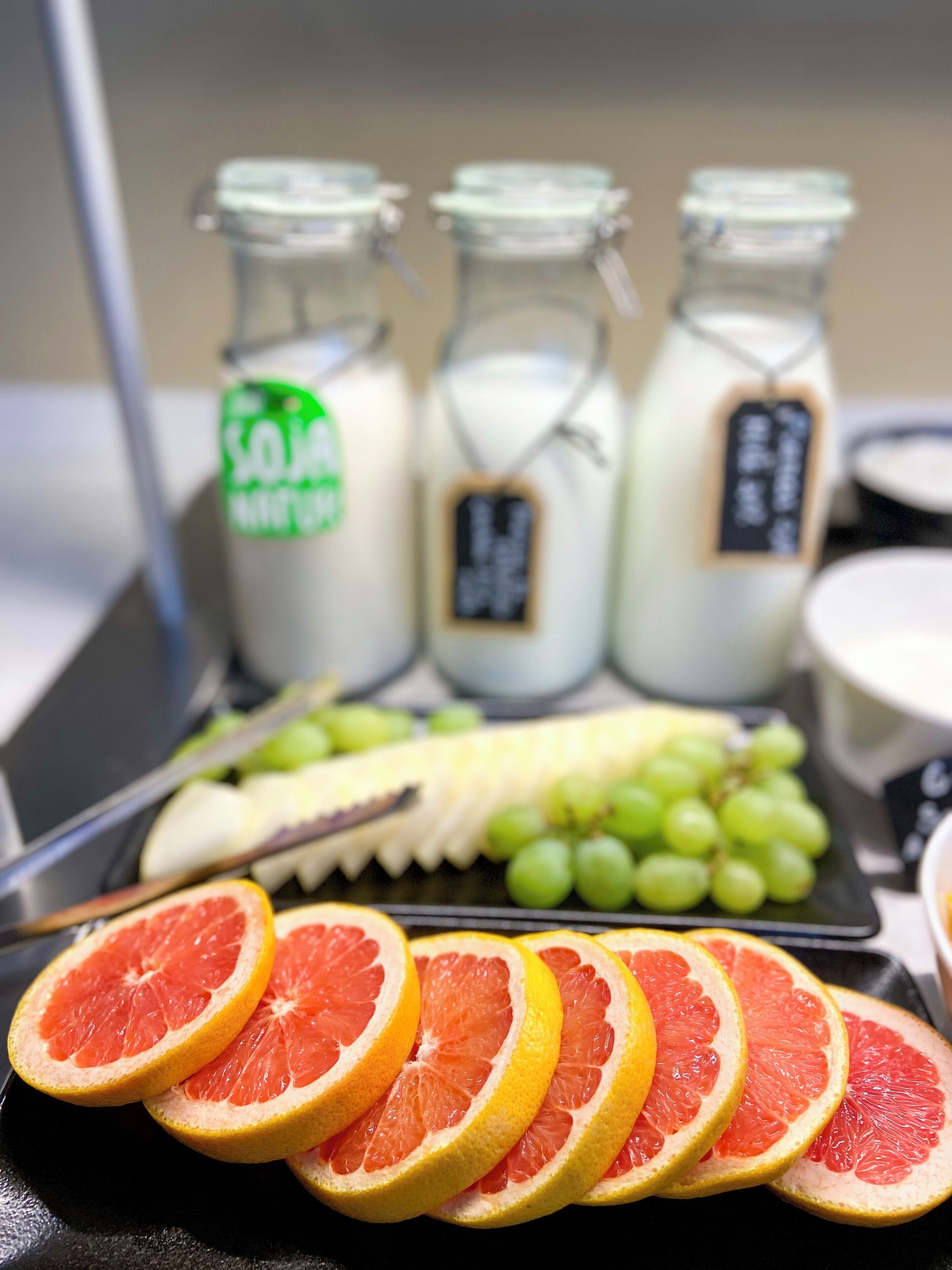 Una bandeja con rodajas de naranja, uvas y un plátano. Se observan tres botellas de vidrio con etiquetas al fondo.