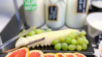 A tray with sliced oranges, grapes, and a banana. There are three glass bottles with labels in the background.