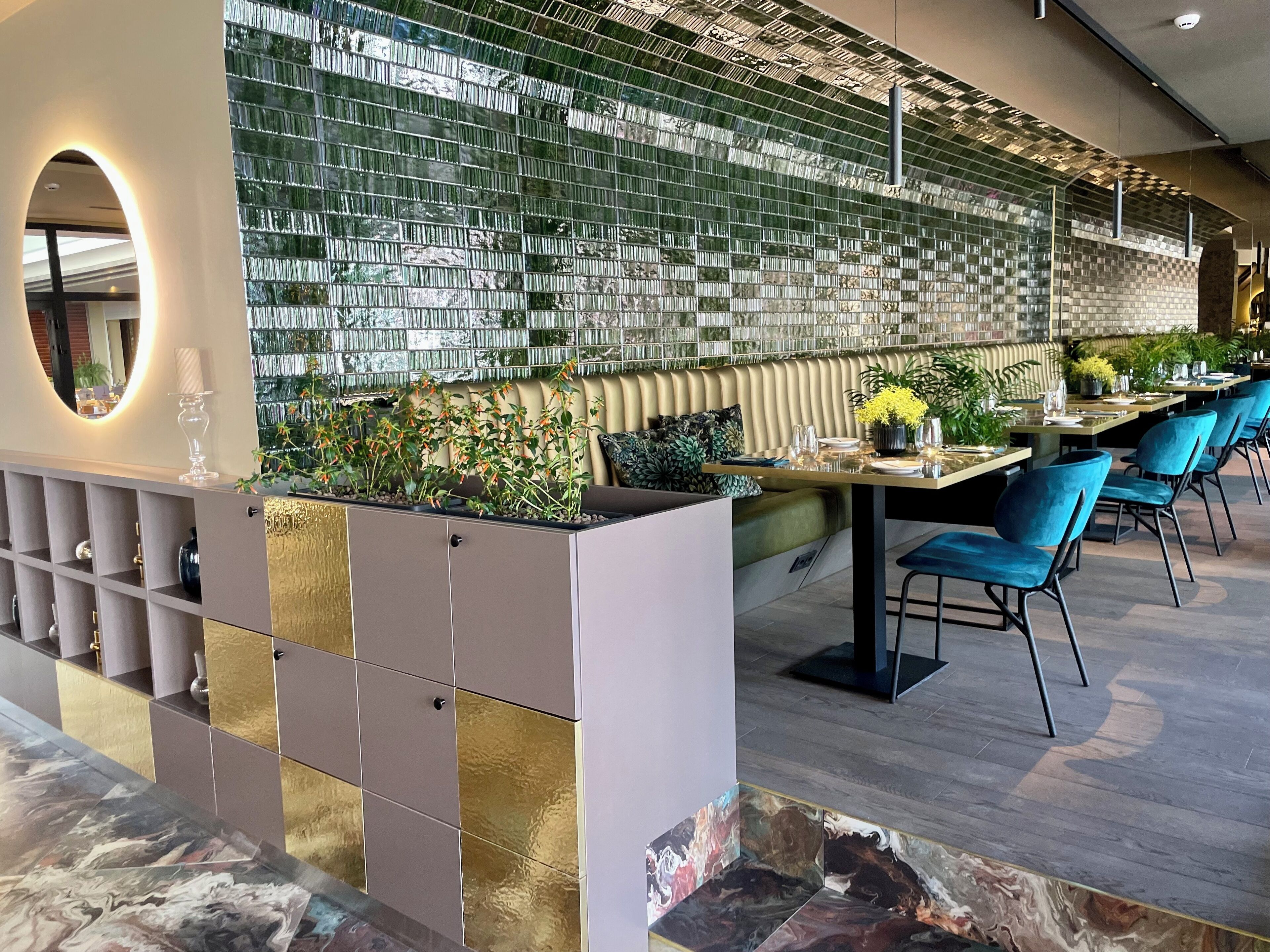 Interior moderno de restaurante con un muro divisor de vidrio, zona de estar y un arreglo decorativo de plantas.
