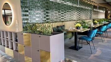 Interior moderno de restaurante con un muro divisor de vidrio, zona de estar y un arreglo decorativo de plantas.