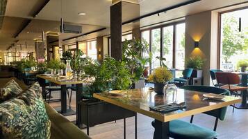 Un interior de restaurante moderno con techos altos, ventanas amplias y plantas de interior.