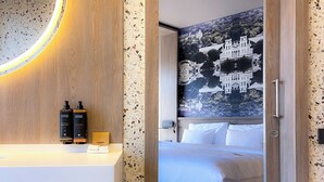 Ein Hotelzimmer mit Holztür, einem Spiegel mit runder Beleuchtung, einem Bett mit weißer Bettwäsche und einem Wandbild.