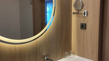 A bathroom with a wooden vanity, a round mirror with a light, a sink, and a towel rack.