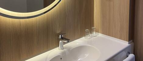 Une salle de bain avec un meuble-lavabo en bois, un miroir rond avec un éclairage intégré, un lavabo et un porte-serviettes.