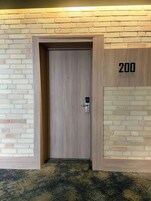 Entrada a una habitación de hotel con una puerta de madera, el número '200' en la pared y una alfombra estampada.
