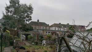 A residential backyard with a paved area, a wooden shed, and a variety of plants and trees. - 3 Minutes to Train station large town house with 5 bedroom, 6 bed, sleep 8 guest (Ilford)