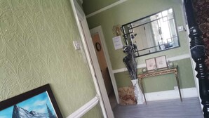 A hallway with patterned wallpaper, a radiator, a framed painting, a mirror, and a console table with decorative items. - 3 Minutes to Train station large town house with 5 bedroom, 6 bed, sleep 8 guest (Ilford)