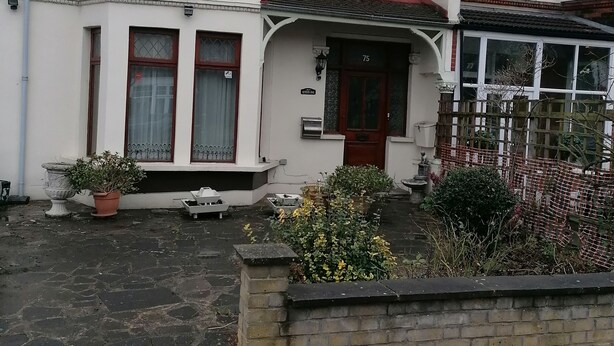 A two-story house with a red door, a number '75' sign, and a garden area with potted plants and a brick wall. - 3 Minutes to Train station large town house with 5 bedroom, 6 bed, sleep 8 guest (Ilford)
