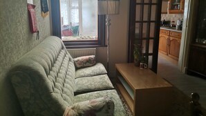 A living room with a sofa, a coffee table, a lamp, and a view of a kitchen through an open door. - 3 Minutes to Train station large town house with 5 bedroom, 6 bed, sleep 8 guest (Ilford)