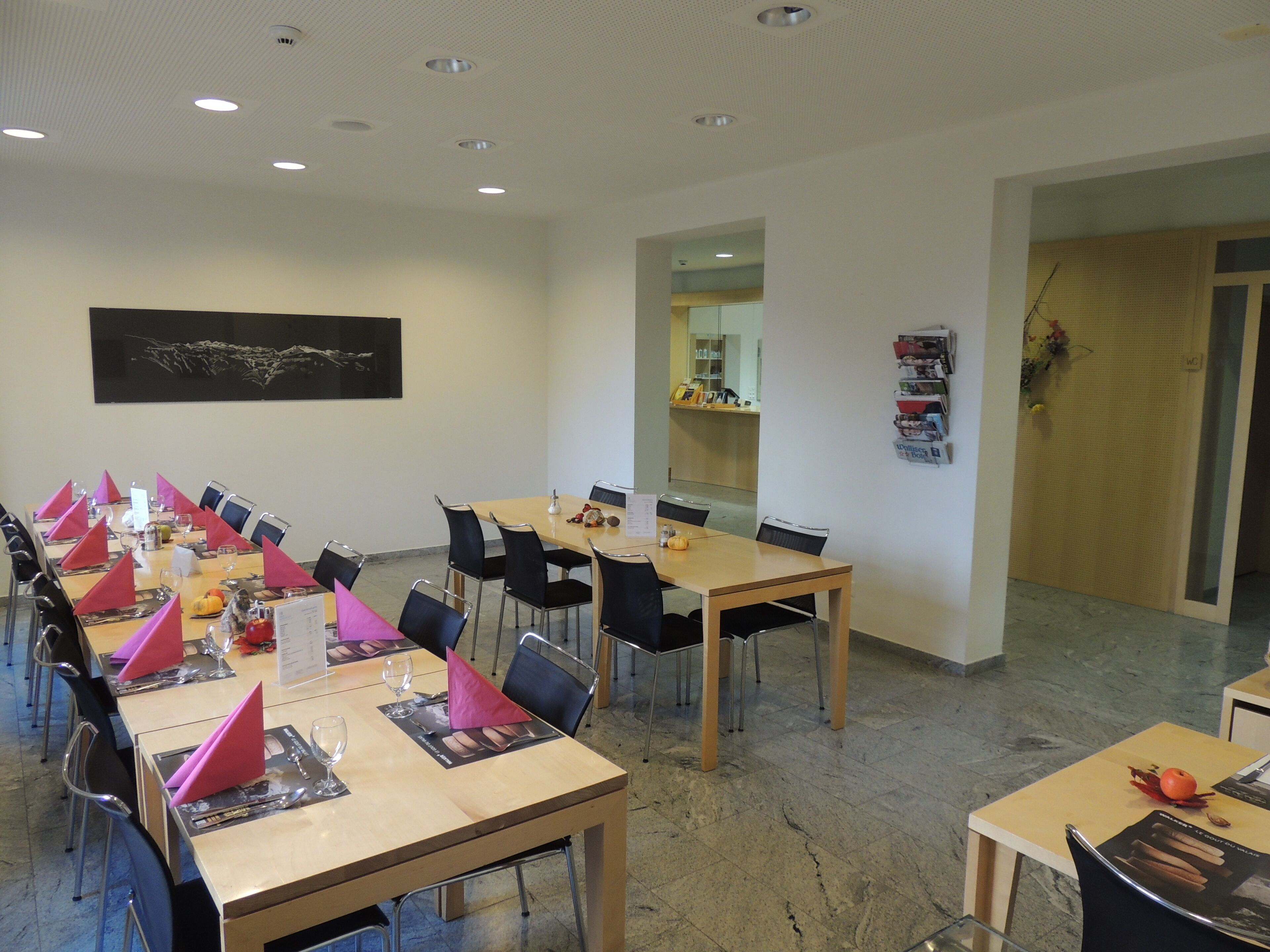 A conference room with multiple tables set for meetings, equipped with chairs, tables, and a large painting on the wall.