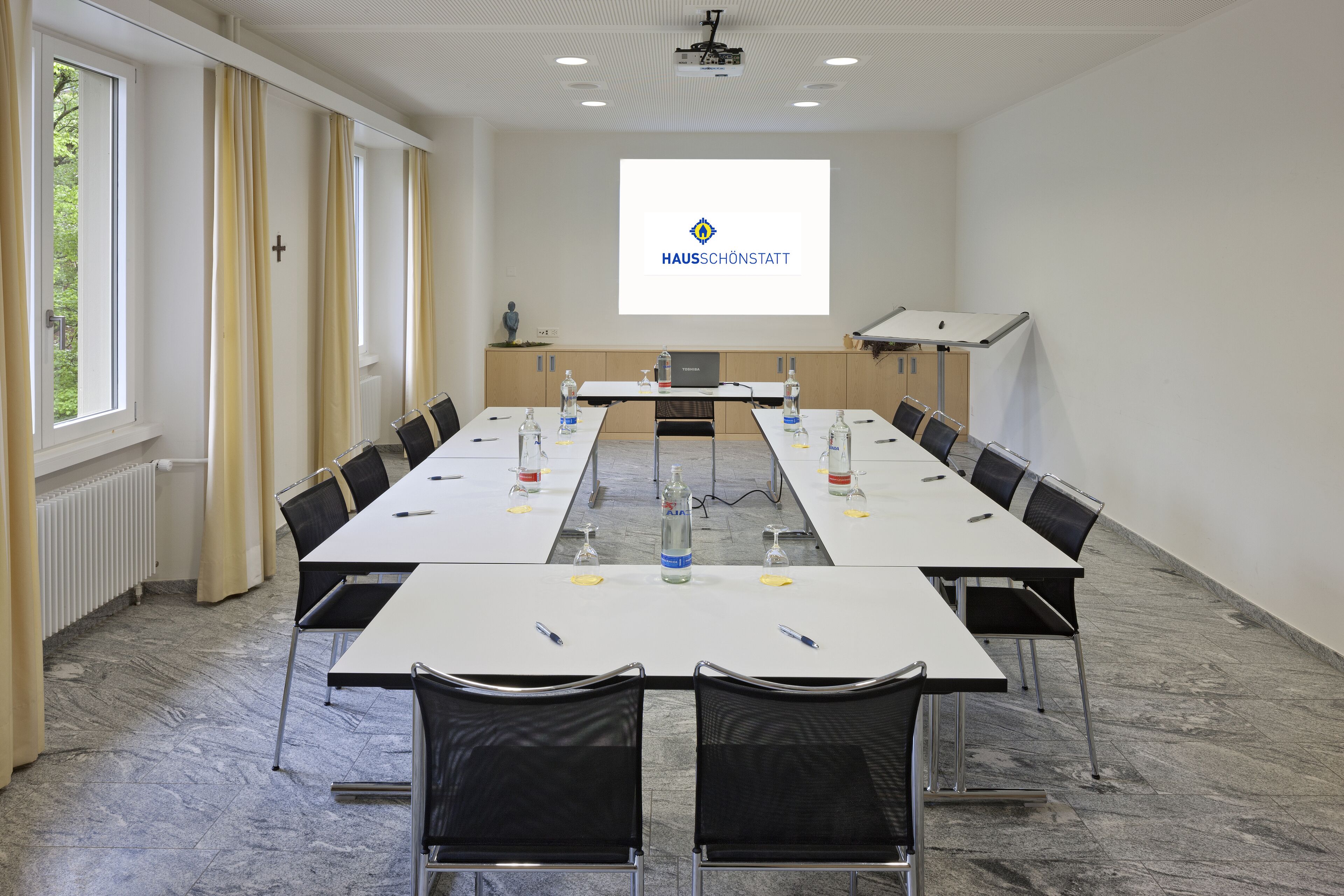 A conference room with a long table, chairs, a projector screen, and a podium.