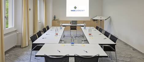 A conference room with a long table, chairs, a projector screen, and a podium.