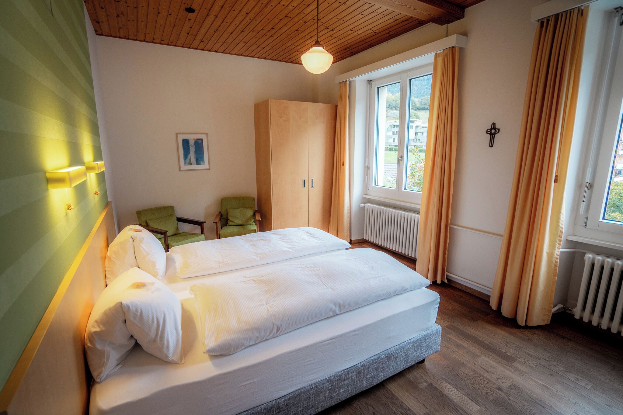 Un dormitorio con cama, una silla, un armario y un ventanal con cortinas.