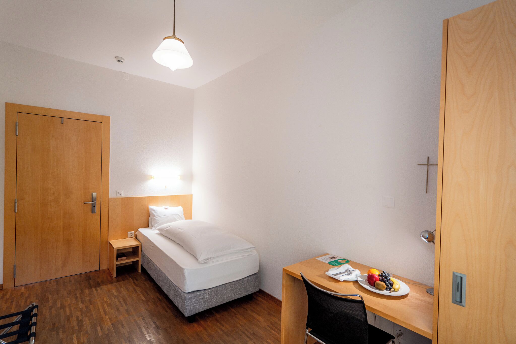 Habitación de hotel con cama, escritorio con silla, mesita y una bandeja de frutas.