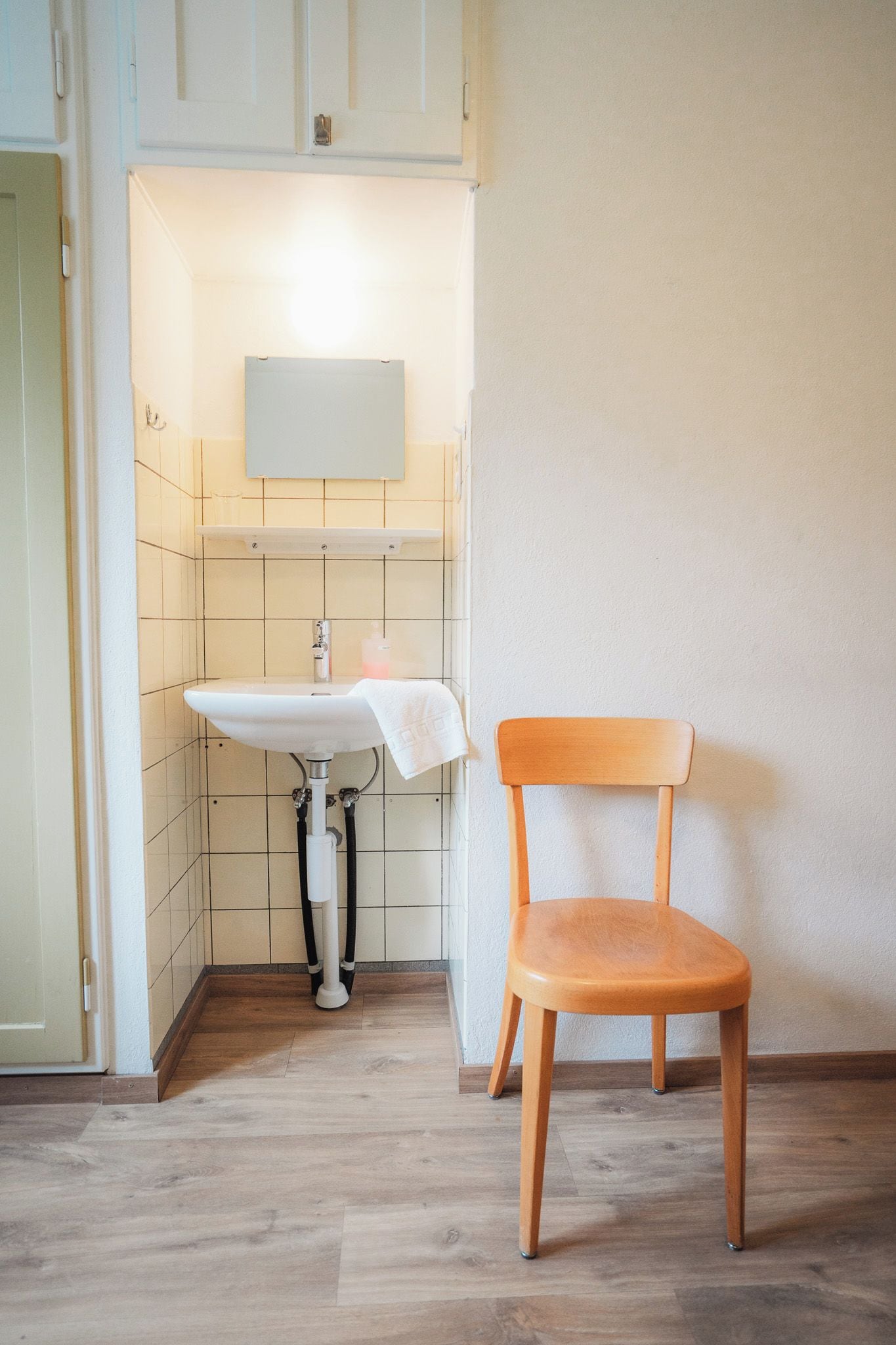 A bathroom with a sink, a mirror, and a wooden chair.
