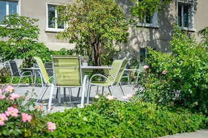 An outdoor seating area with a table and chairs, surrounded by lush greenery and flowering plants.