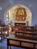 A church interior with pews, a stained glass window, and a central altar with religious statues and candles.