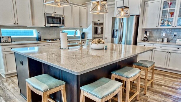 A kitchen with a large island, bar stools, stainless steel appliances, and pendant lighting.