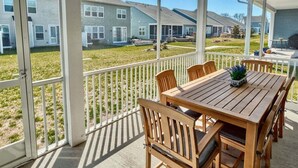 A covered patio with a wooden table and chairs, a white railing, and a view of residential buildings.