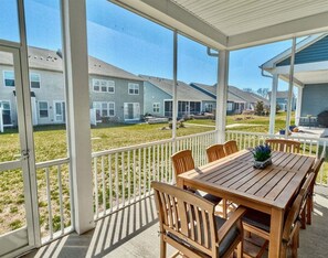Eine überdachte Terrasse mit einem Holztisch und Stühlen, einem weißen Geländer und Blick auf Wohnhäuser.