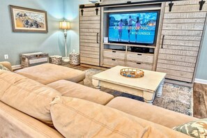 A living room with a large flat-screen TV, a wooden entertainment unit, a beige sofa, and a coffee table. - Ocean View * 5BR Luxury Beach Resort Home (Ocean View)