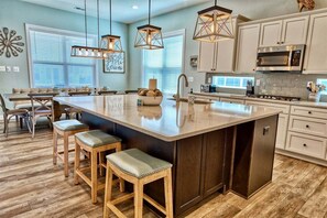 A kitchen with a large island, wooden stools, pendant lights, and a microwave. - Ocean View * 5BR Luxury Beach Resort Home (Ocean View)