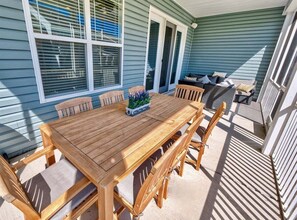 Ein Holztisch mit Stühlen, ein Topfpflanze und eine Couch auf einer überdachten Terrasse.