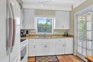 A kitchen with white cabinets, a granite countertop, a built-in oven, and a window with blinds.