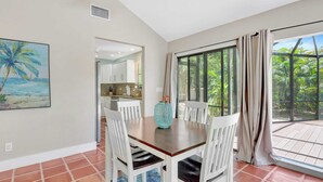 A dining area with a table and chairs, a kitchen in the background, and a large window with curtains. - A Private Oasis Complex in Naples (Naples)