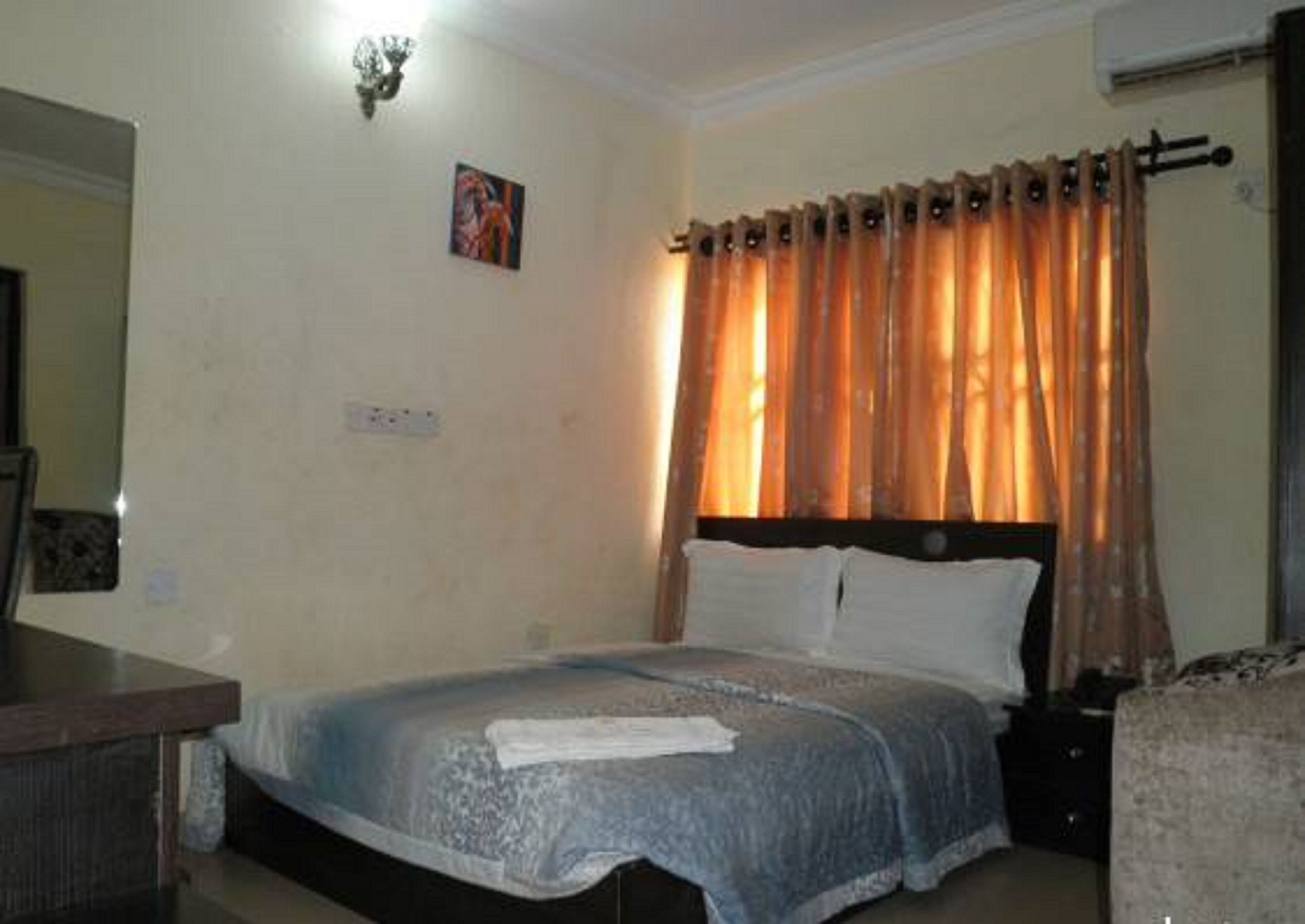 A bedroom with a bed, a nightstand, a dresser, and a wall-mounted light fixture.
