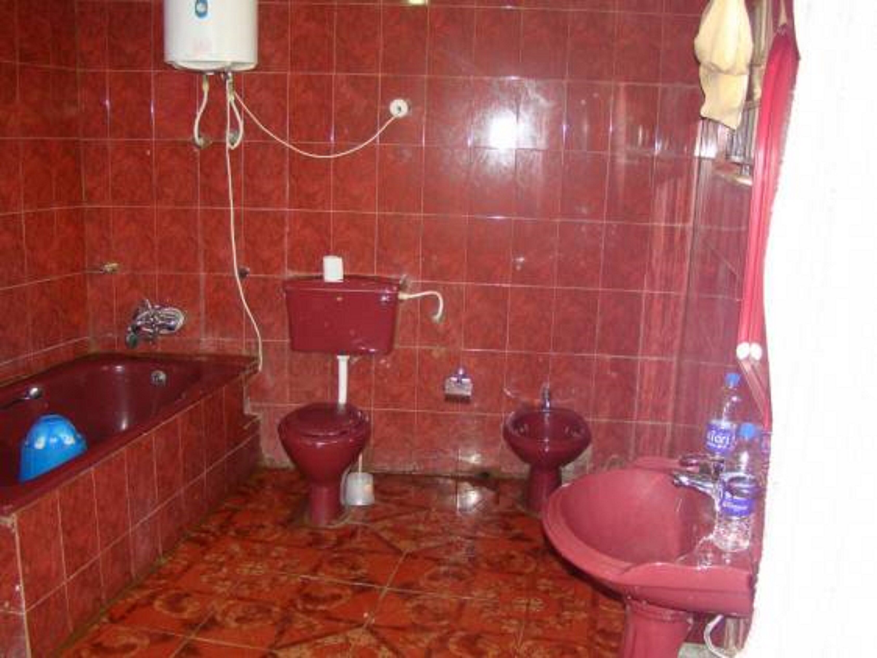 A bathroom with a red tiled floor, a bathtub, two toilets, and a sink.