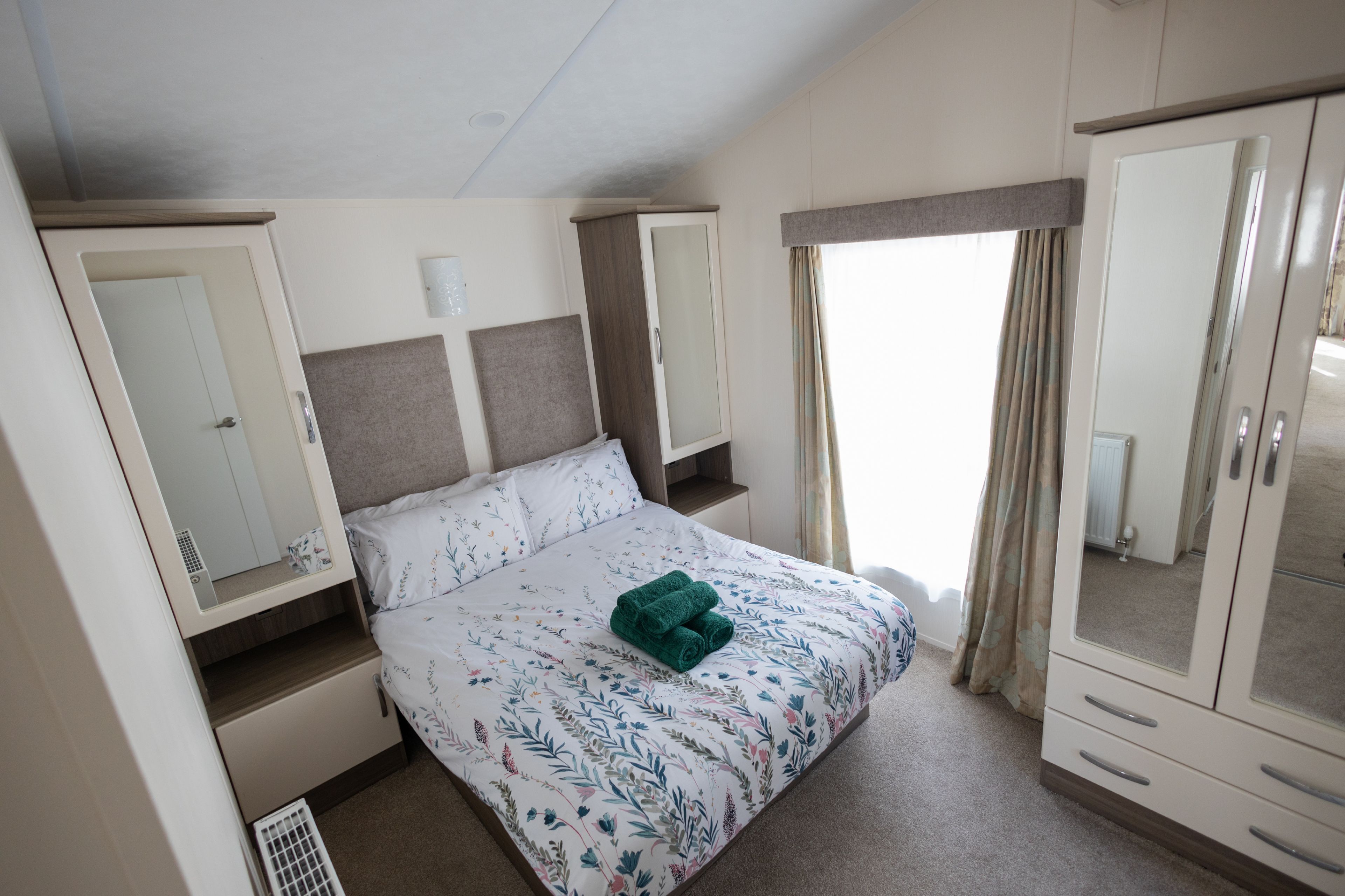 Une chambre à coucher avec un lit, une armoire, un miroir et une fenêtre avec des rideaux.