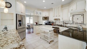 A modern kitchen with white cabinetry, stainless steel appliances, a granite countertop, and a central island.