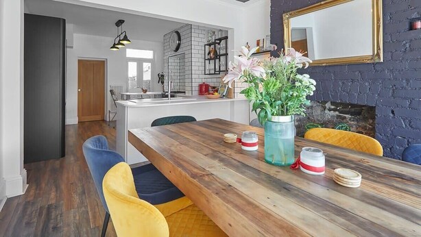 Une cuisine moderne avec un mur de fond en briques, une table à manger en bois et des chaises jaunes.