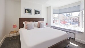 Une chambre d’hôtel avec un grand lit, une vue sur la ville par la fenêtre et une petite table de chevet avec une lampe.