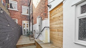Une ruelle étroite avec un banc en bois, une porte et une fenêtre dont le vitrage est dépoli.