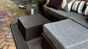 A covered outdoor seating area with a brick wall, a sofa with striped cushions, and a table with chairs. - Brewery District Homestead  (Columbus)