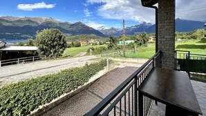 A balcony with a view of a mountainous landscape, a paved area with greenery, and a building with a stone pillar. - Sonhozinho House Colico, Beautiful Villa with Lake and Mountain View (Lombardia)